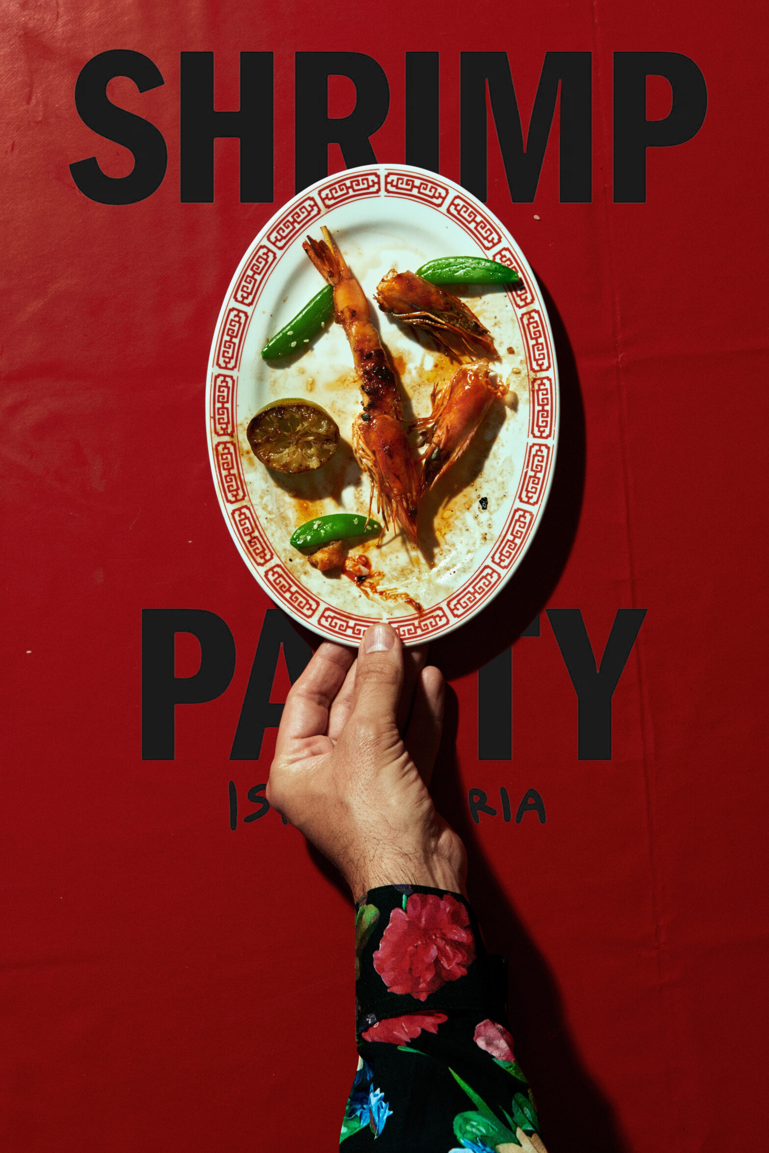 Graphic work of a male hand pushes an almost finished plate of shrimps over red tablecloth.