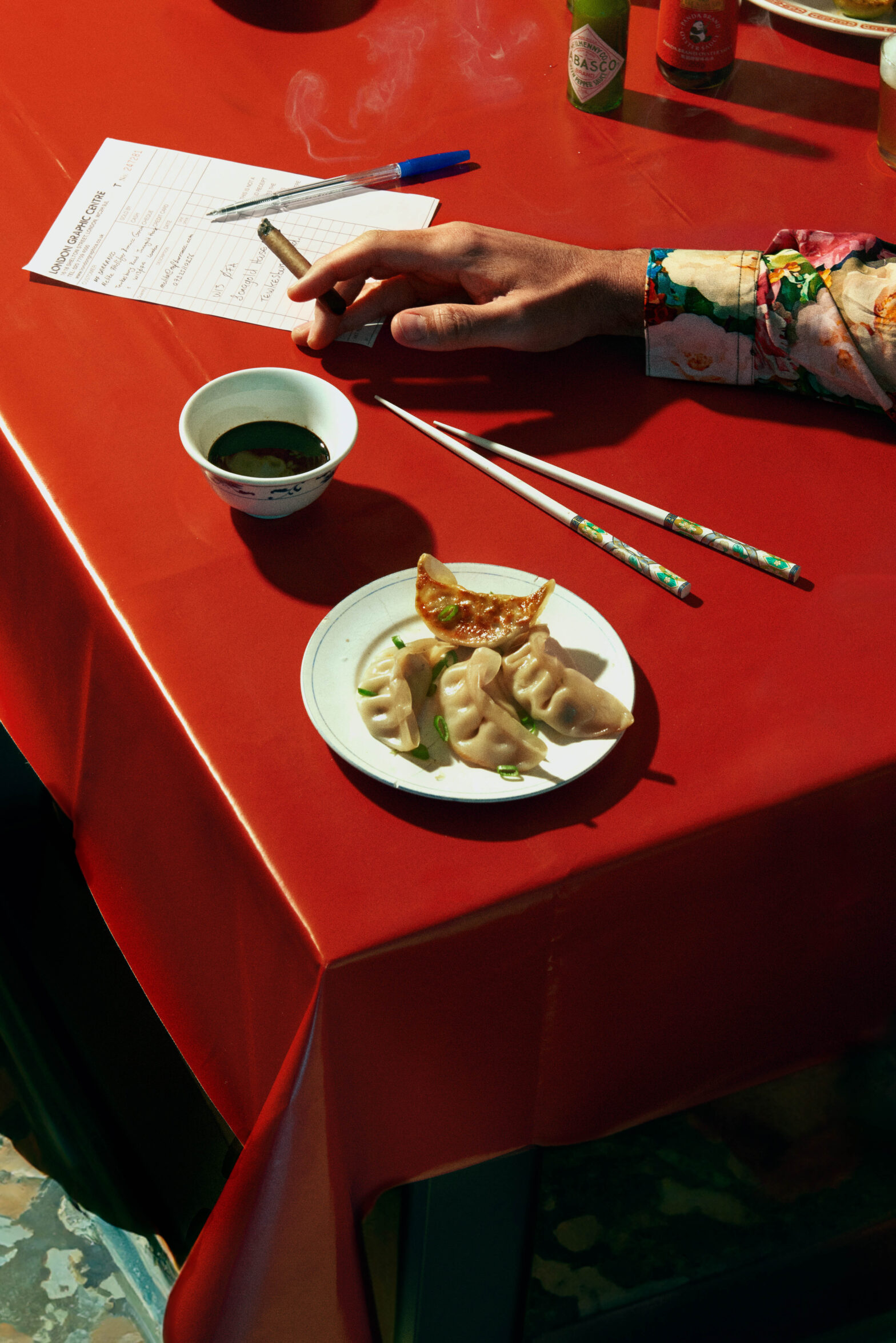 Male hand smoking cigar at the chineese restaurant table next to a plate of gyozas.